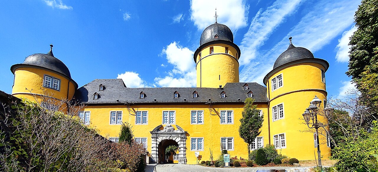 Schloss Montabaur mit gelber Fassade und drei Türmen unter blauem Himmel