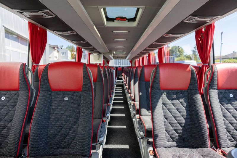 Innenraum eines Reisebusses mit roten Ledersitzen, Mittelgang und Vorhängen